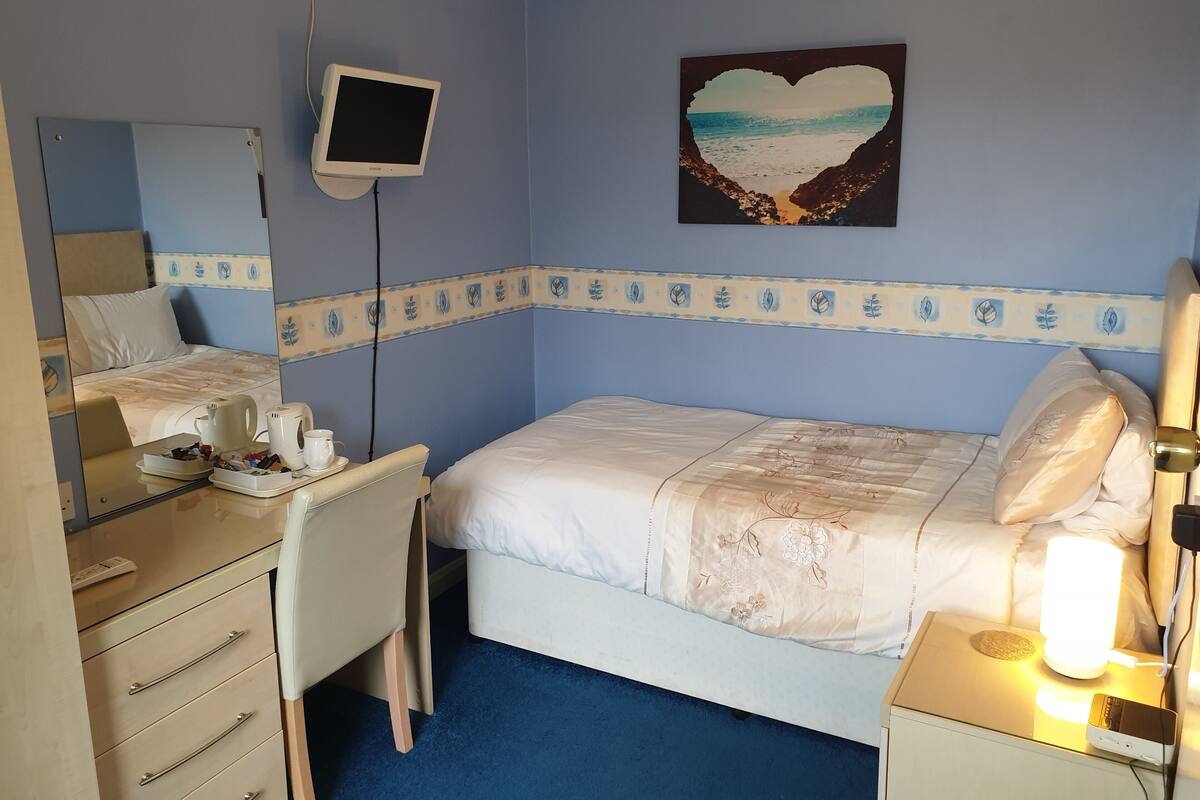 A hotel room with a bed, bedside table, desk, chair, and a TV mounted on the wall.