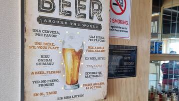Un mur sur lequel est affiché un panneau indiquant différents noms de bières dans différentes langues, un panneau interdisant de fumer et un autre indiquant les prix des boissons alcoolisées.
