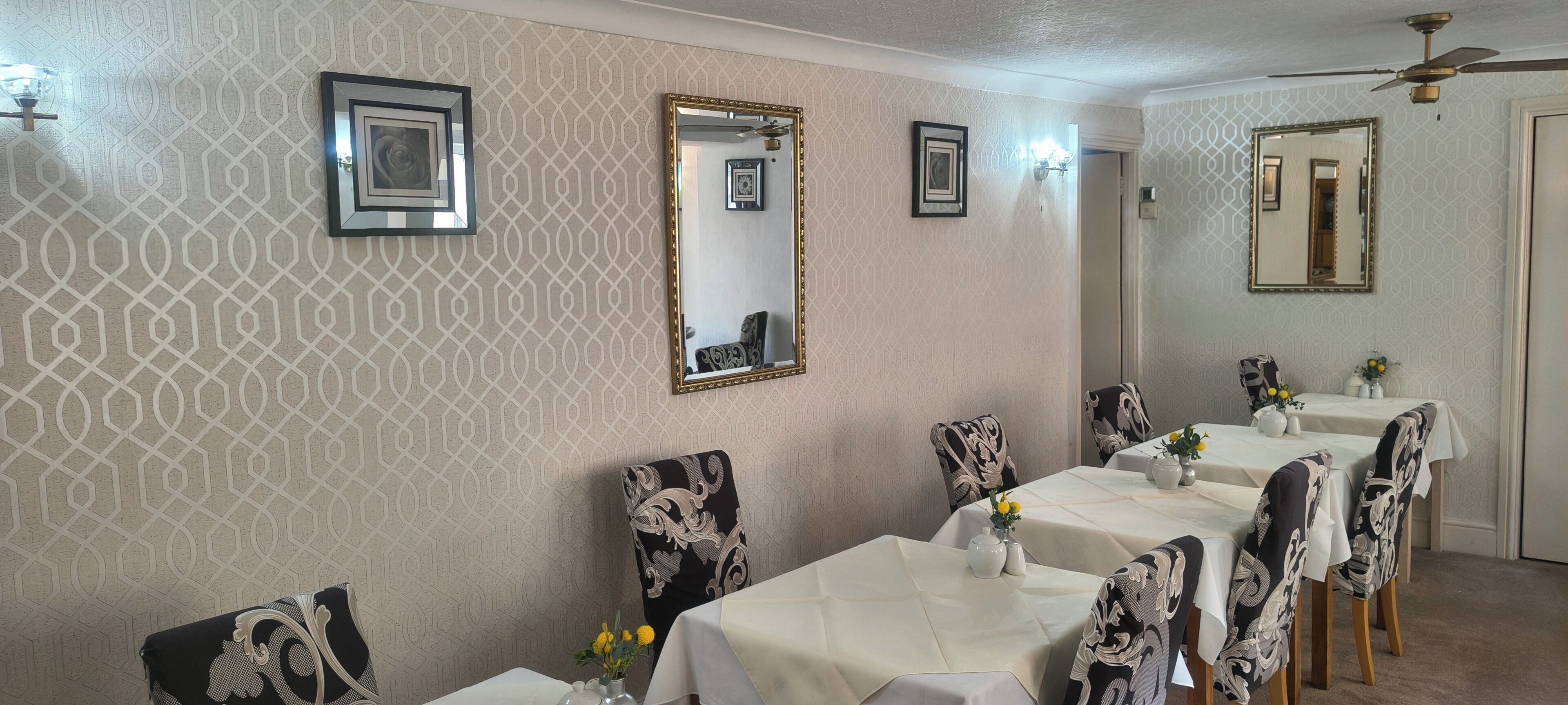 Un comedor con pared decorada, espejos enmarcados y ventilador de techo.