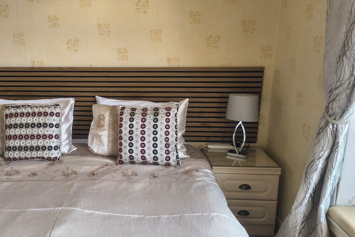 A neatly made bed with patterned pillows, a bedside lamp, and a nightstand with a lamp.