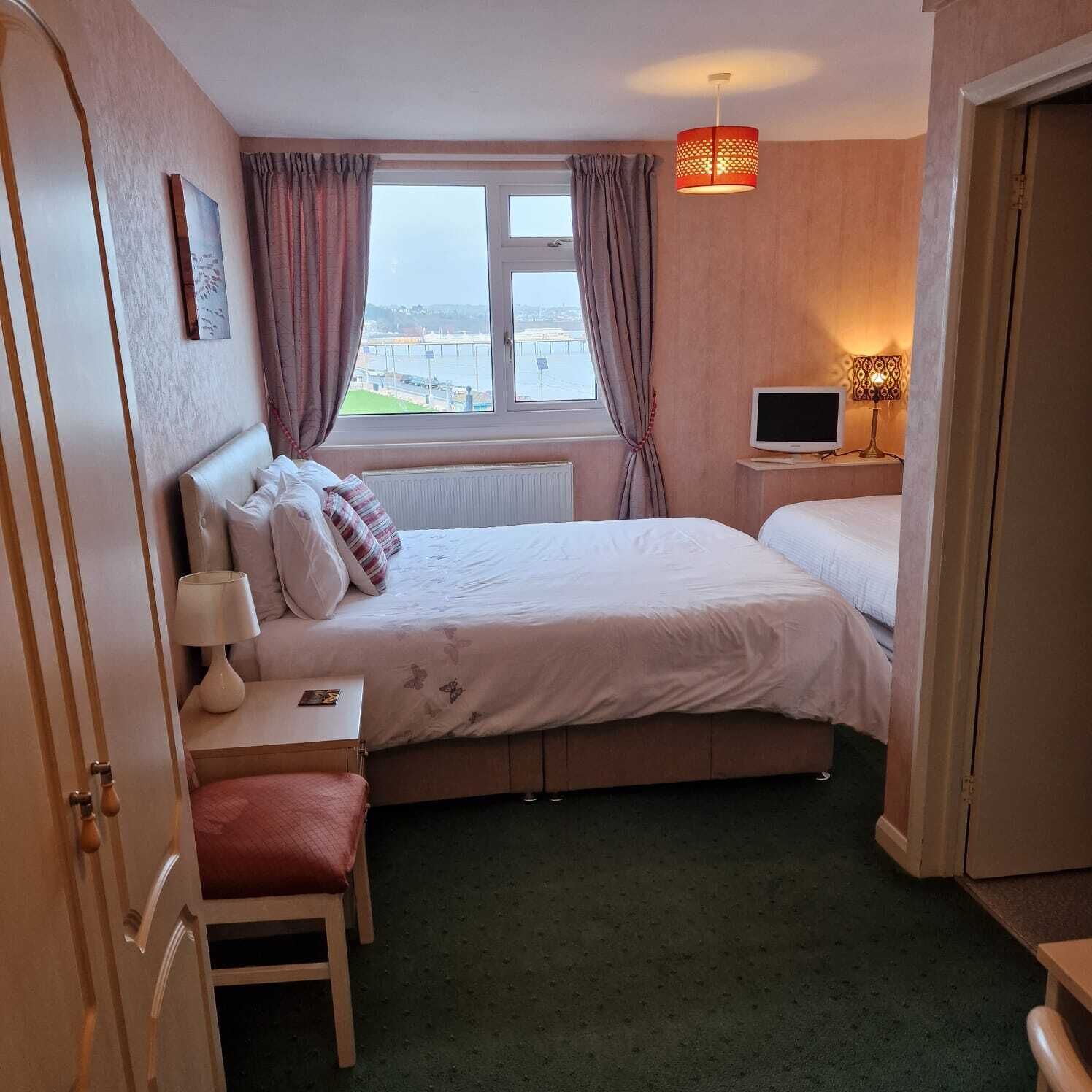 A hotel room with a bed, a desk, a chair, a TV, and a window with curtains.