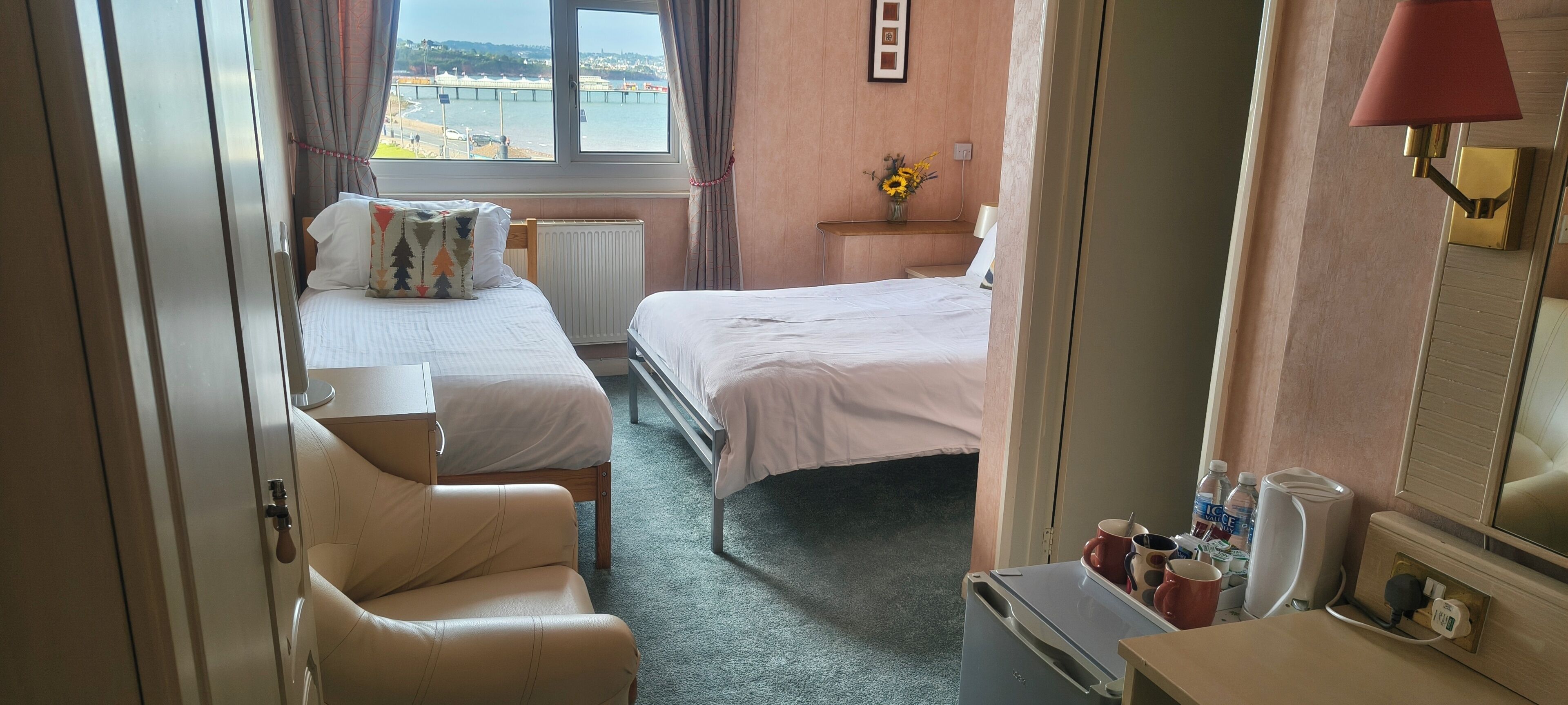 Quarto de hotel com duas camas, um espaço de estar, janela com vista e mesa de cabeceira com abajur.