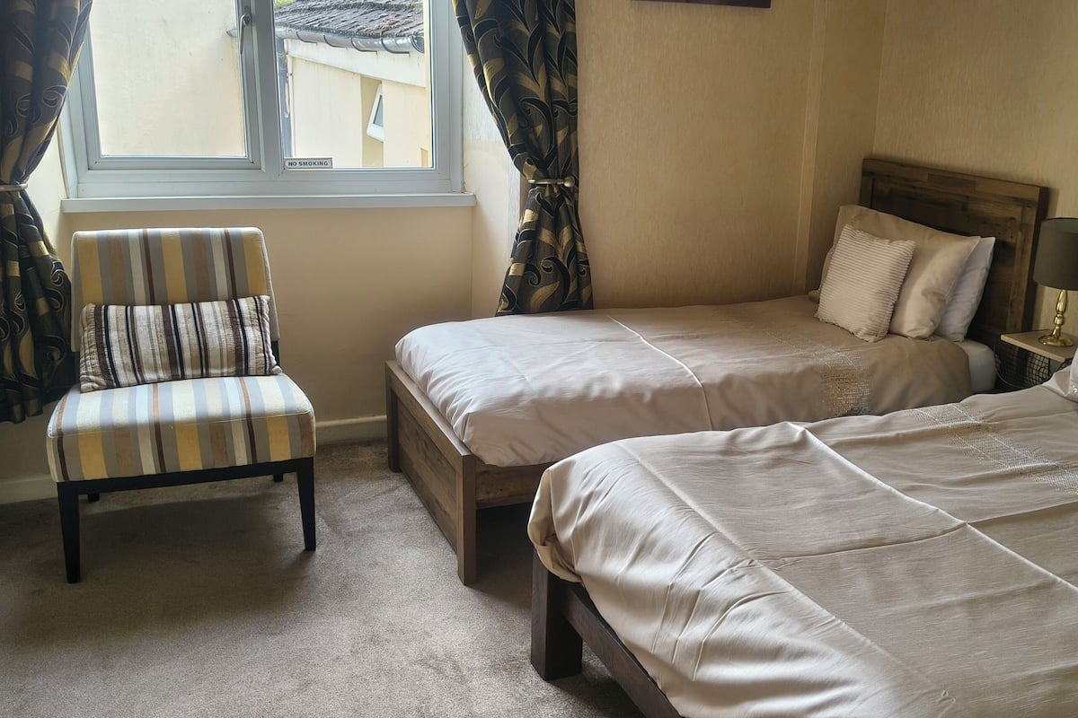 A hotel room with two beds, a chair, a window with curtains, and a lamp on the nightstand.