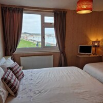 A hotel room with a bed, a TV, a window with curtains, and a view of a bridge and water.