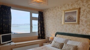 A hotel room with a bed, a TV, a window with curtains, a lamp, and a framed picture on the wall. - The Sands Hotel (Paignton)