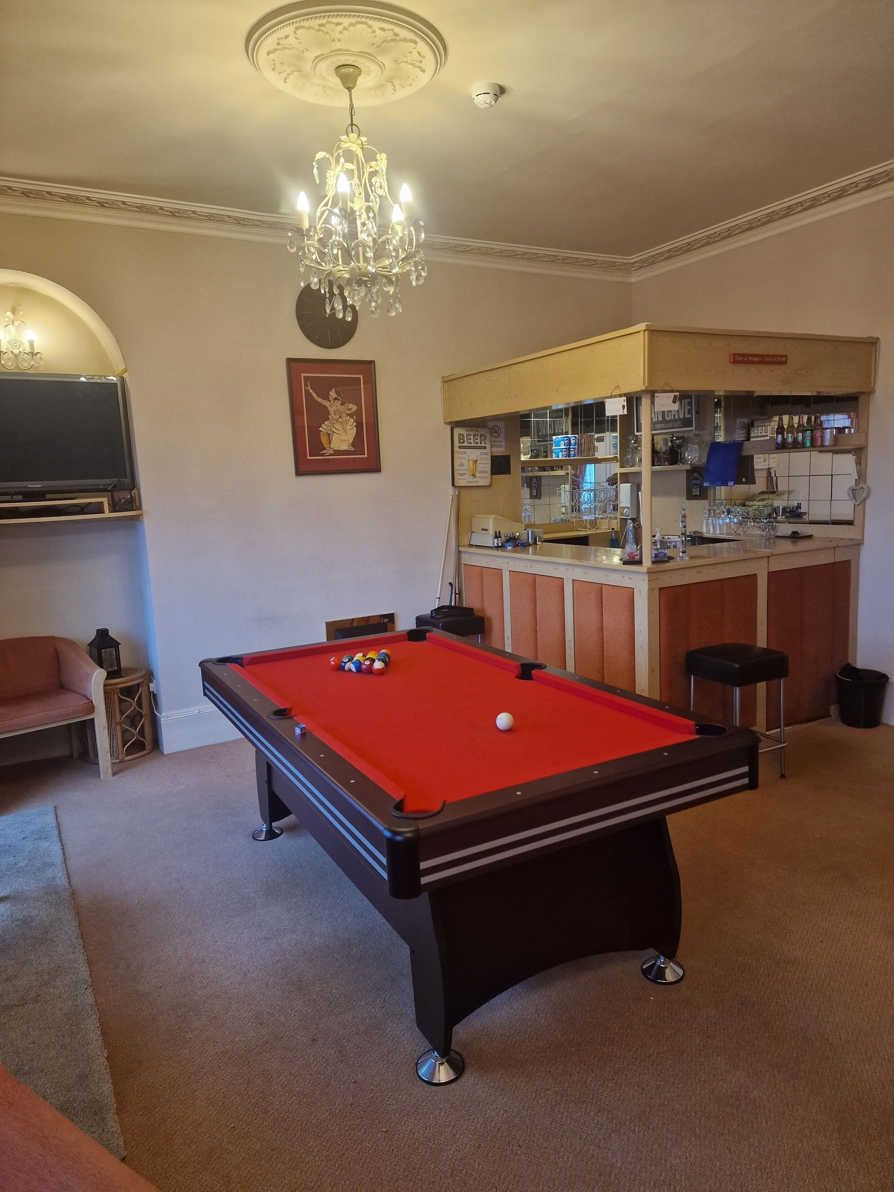 Una mesa de billar con bolas, una zona de bar con botellas, un televisor y un candelabro.