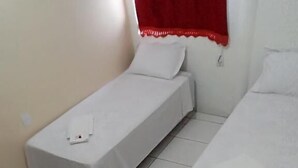 A room with three single beds, each with a white bedspread and a pillow.