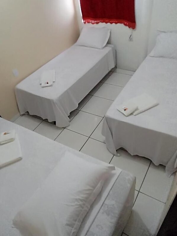Une chambre avec trois lits simples, chacun étant recouvert d’une courtepointe blanche et muni d’un oreiller.