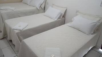 Três camas de solteiro num quarto com roupa de cama e parede brancas.