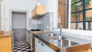 A modern kitchen with a black and white checkered floor, stainless steel appliances, and a window with a view of greenery. - B&B Hart van Leiden (Leiden)