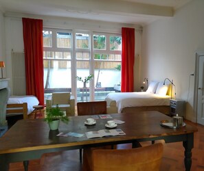 A hotel room with a bed, a dining table with chairs, a small table with a plant, and a window with red curtains. - B&B Hart van Leiden (Leiden)