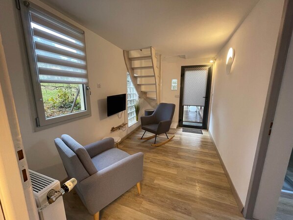 Uma sala de estar moderna com um sofá cinza, uma TV e piso de madeira.