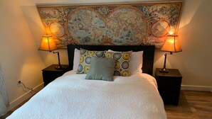 A neatly made bed with a white duvet, two bedside lamps, and a world map tapestry above it. - Country Getaway near Seattle (Maple Valley)