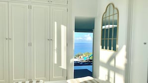 Quarto com cama, duas almofadas, janela com vista para o mar e porta para uma varanda.