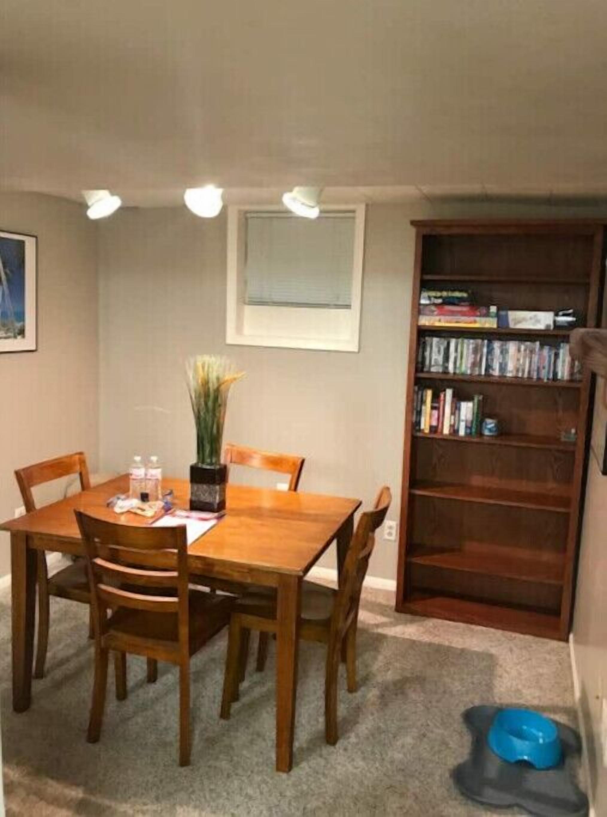 A dining area with a wooden table and chairs, a bookshelf, and a pet bowl on the floor.