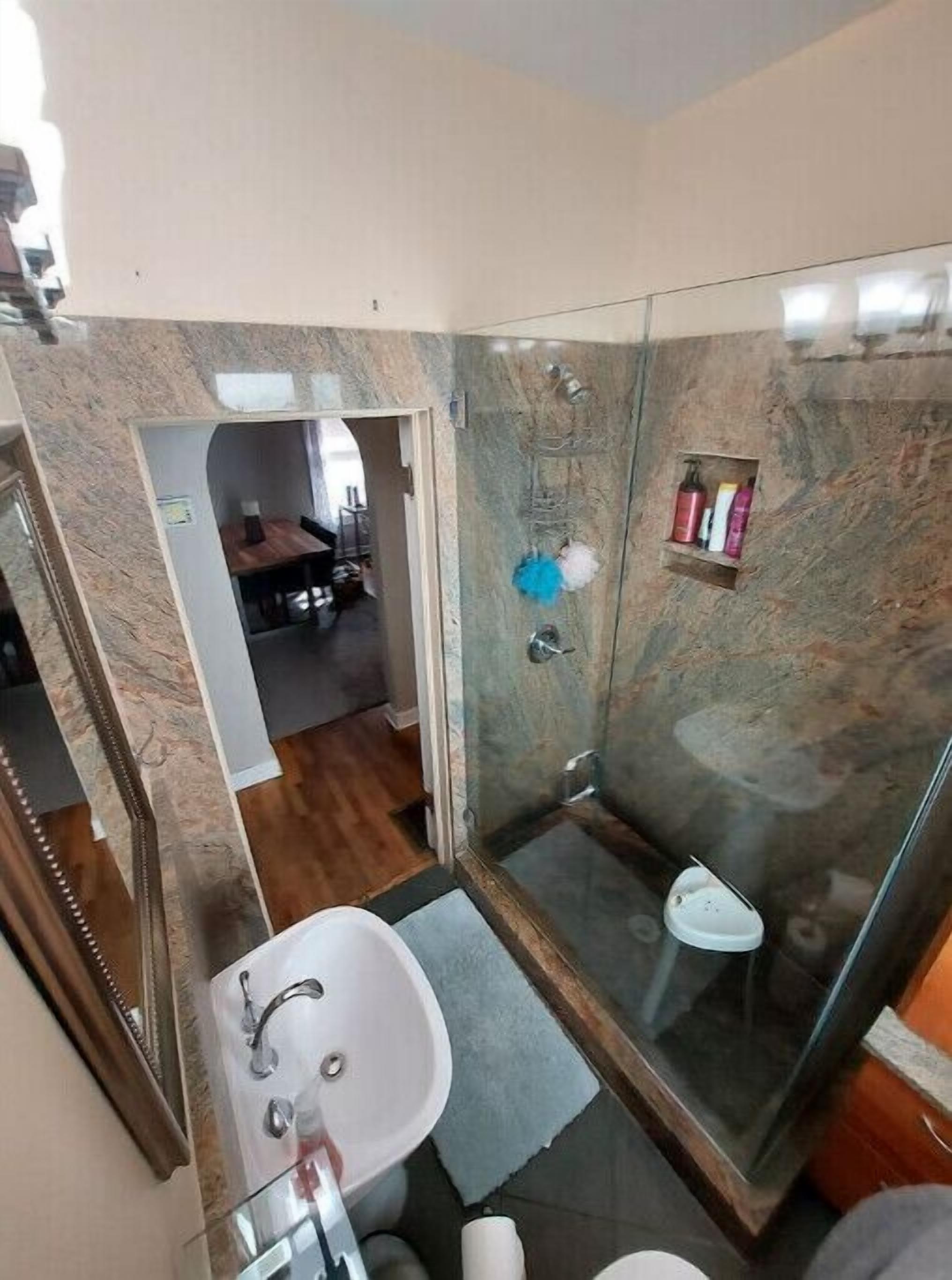 Een moderne badkamer met een douchecabine van glas, een witte wastafel en een klein plankje met toiletartikelen.