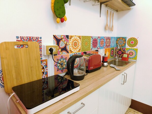 A kitchen with a wooden countertop, a toaster, a kettle, and colorful tiles on the backsplash.