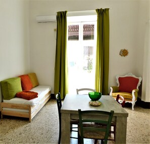 A room with a wooden sofa, a dining table with chairs, and a window with curtains.