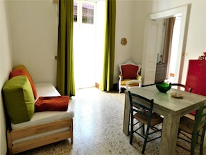 A room with a wooden bed, a dining table with chairs, a red chair, and a green bowl on the table.
