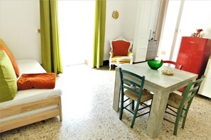 A room with a bed, a dining table with chairs, a red refrigerator, and a chair with a red cushion.