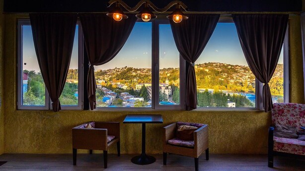 A room with a view of a hillside town, two wicker chairs, a small table, and a hanging light fixture. - Green flower is located in the historical part of Kutaisi.5-minute walk  centre. (Kutaisi)