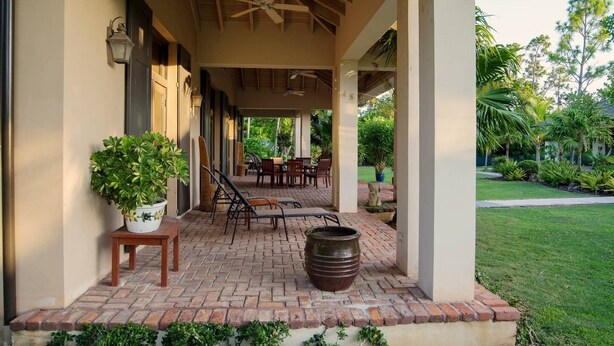 Een overdekte terras met bakstenen vloer, loungesteilen en een grote plantenbak.