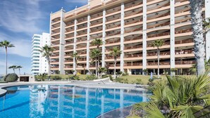 Un hotel de varios pisos con balcones, piscina y palmeras.