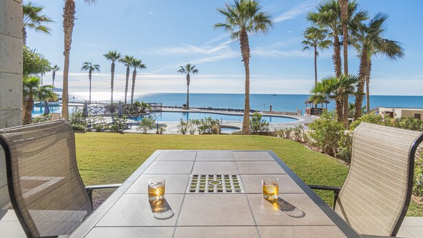 Un patio con dos sillas y una mesa, con vista a una piscina y al océano.