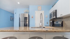 Una cocina moderna con un refrigerador de acero inoxidable, una cafetera, un microondas y un lavamanos. Hay tres taburetes altos frente al lavamanos.