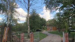 Een verhard pad dat leidt naar een toegangspoort met een houten bord waarop 
