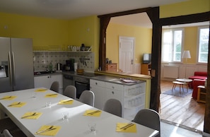 Ein Essbereich mit einem weißen Tisch, gedeckt für sechs Personen, eine Küche mit gelben Wänden und ein rotes Sofa im angrenzenden Wohnzimmer.