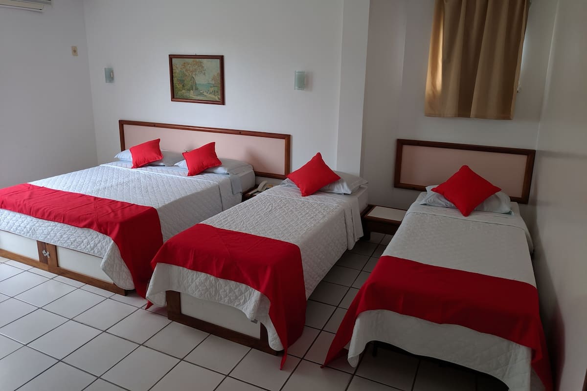 A hotel room with three beds, each with a red and white bedspread, and a painting on the wall.