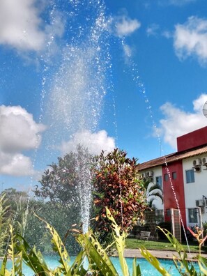 A clear sky with a fountain in the foreground and a building with a red roof in the background.
