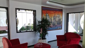 A lobby with red chairs, a potted plant, and a large painting of a ship on the wall. - Hotel Portal de Eunápolis (Eunapolis)