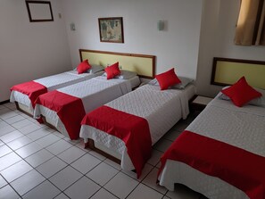 A hotel room with four single beds, each with a red pillow and white bedding.