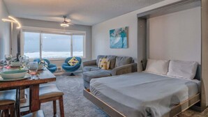 Une chambre moderne avec un lit, un canapé, une table à manger avec des chaises et une vue sur l’océan.