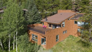 Une maison moderne à deux étages, dotée d’une façade en bois, de grandes fenêtres et d’un balcon aménagé avec des sièges d’extérieur.