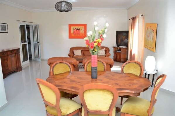 A dining area with a wooden table and chairs, a vase with flowers, and a sofa in the background.