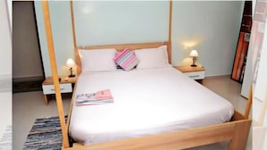 Cama bem arrumada com estrutura de madeira, duas mesas de cabeceira com luminárias, uma gavetinha e uma revista sobre a cama.