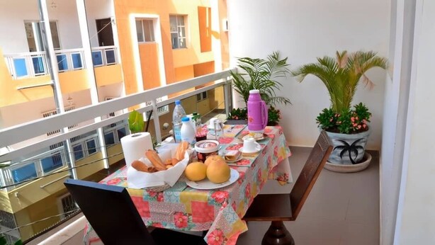 Uma varanda com uma mesa posta para refeição, com pão, frutas e uma garrafa de água.