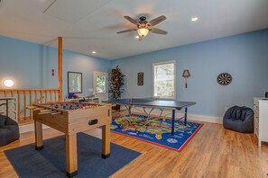 A room with a foosball table, ping pong table, and a dartboard.