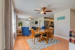 A dining area with a wooden table and chairs, ceiling fans, and a kitchen in the background.