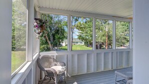Eine überdachte Veranda mit Korbmöbeln, großen Fenstern und einem hängenden Blumenkorb.