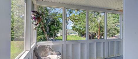 A covered porch with wicker furniture, large windows, and a hanging flower basket.