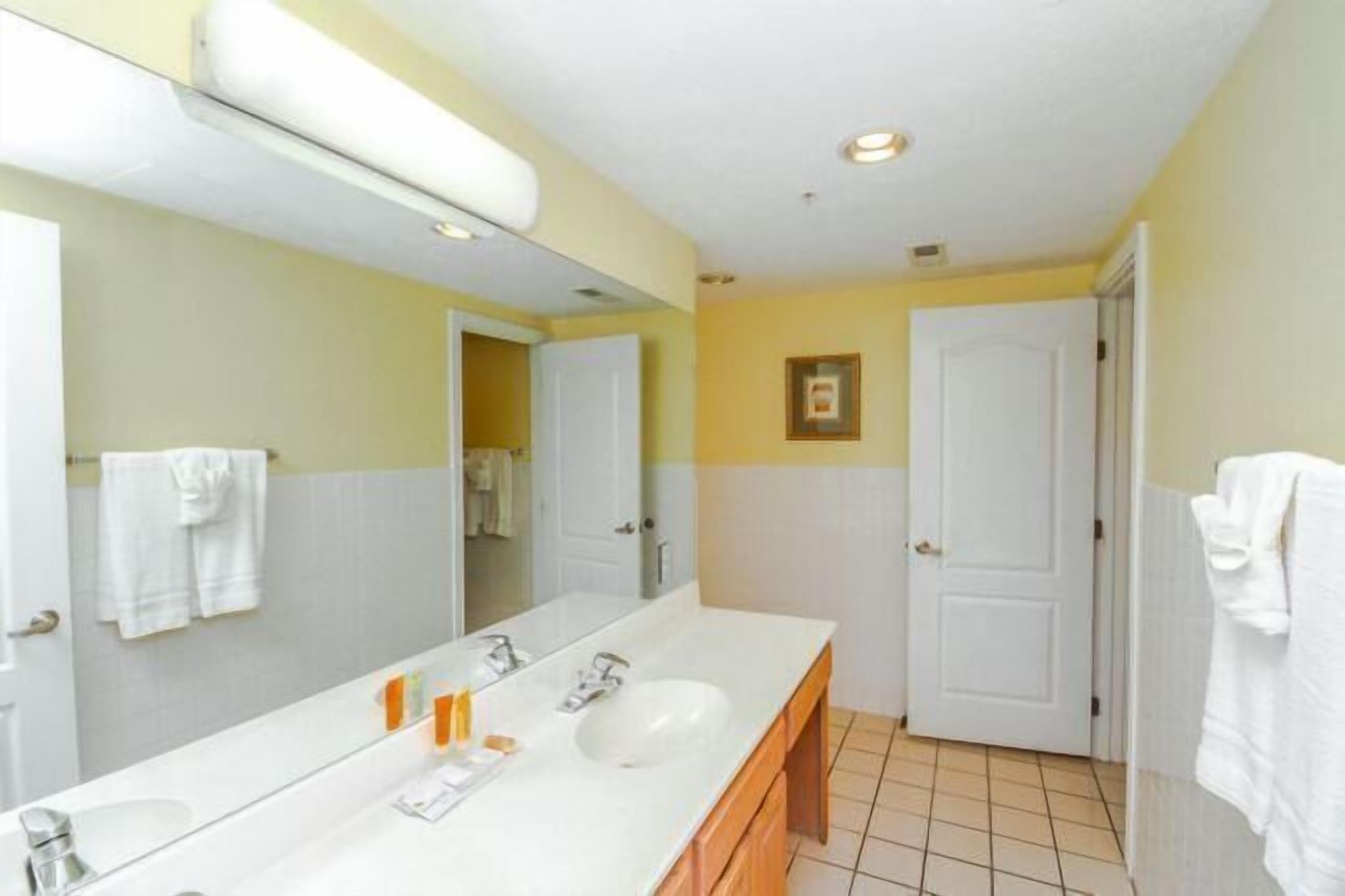 A bathroom with a large mirror, two sinks, and a door.