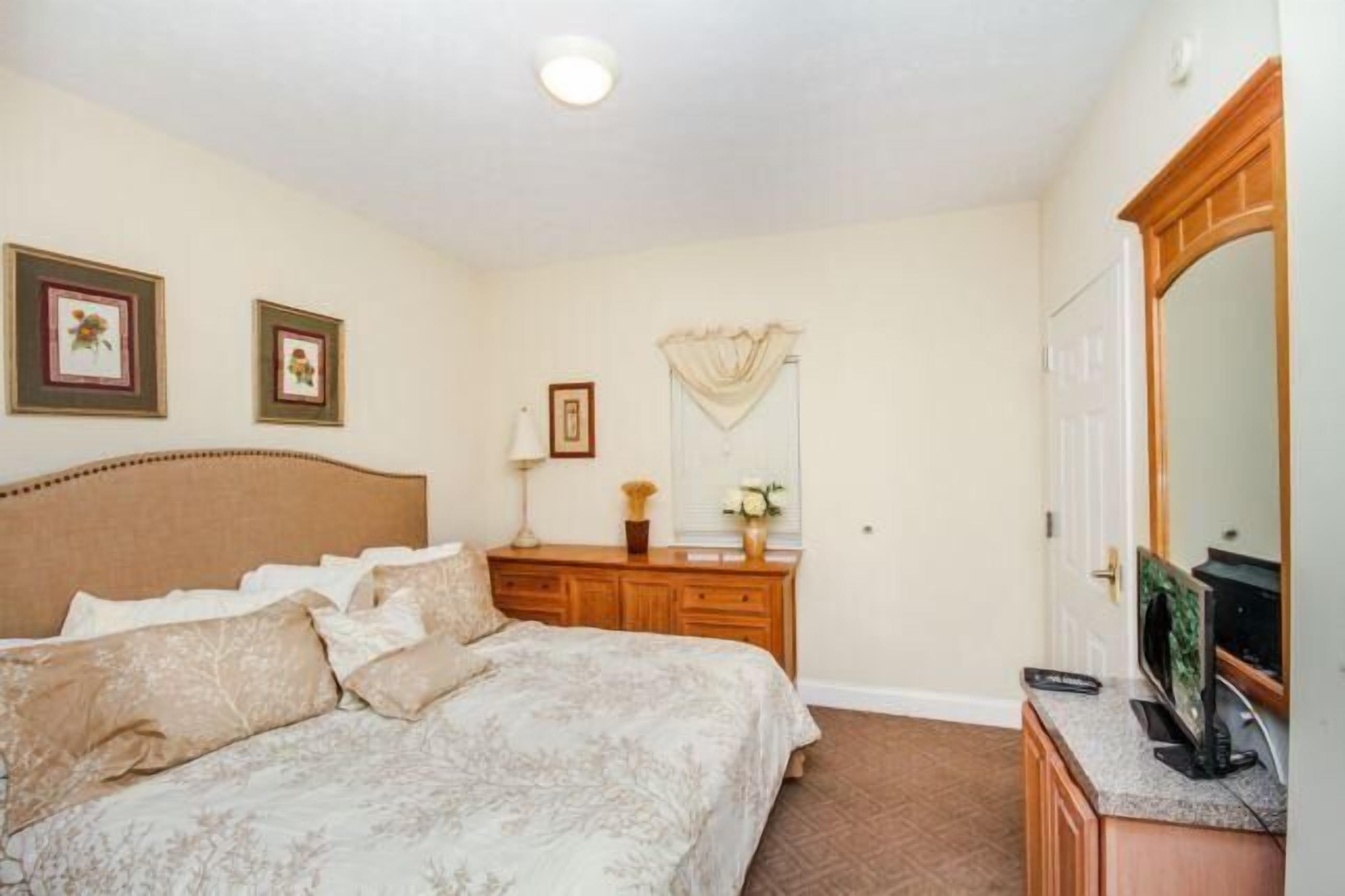 Een slaapkamer met een bed, een dressoir, een spiegel en kunstwerken aan de muur.