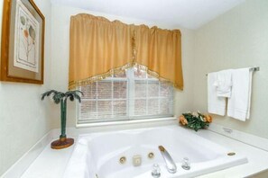 A bathroom with a large bathtub, a window with blinds, a towel rack, and a framed picture on the wall. - 1103 Golf View Towers Smoky Bear (Pigeon Forge)