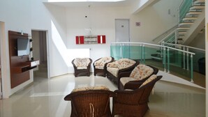 A spacious living area with wicker furniture, a glass railing, and a staircase. - Colonia de Férias Sitraemfa (Peruíbe)