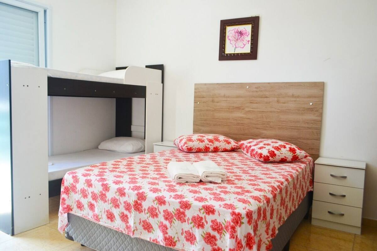 Ein Schlafzimmer mit einem Etagenbett, einem Einzelbett mit floralem Bettbezug, einem Nachttisch und einem Nachtlicht.