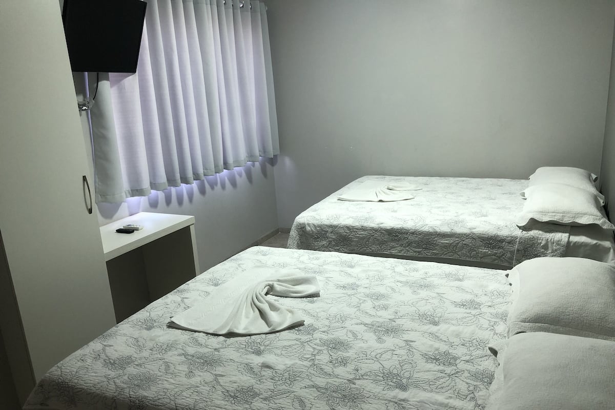 Ein kleines, sauberes Zimmer mit zwei Einzelbetten, einem Nachttisch und einem Vorhang.